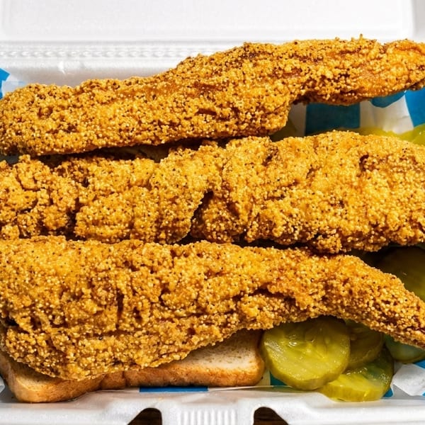 Three pieces of crispy fried fish with pickles and white bread in a takeout container.