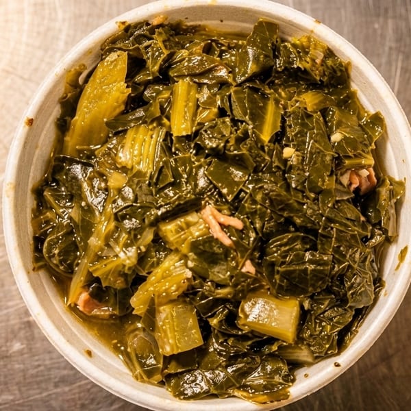 Overhead view of a bowl of dark green collard greens with small pieces of meat.